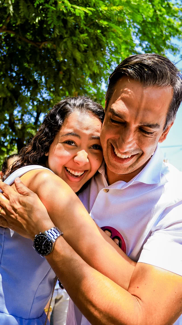 Fábio e uma mulher sorrindo durante um abraço ao ar livre.